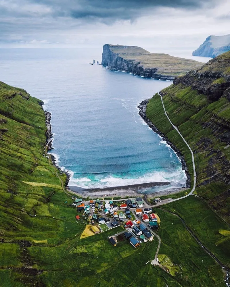 alt: Cảnh quan hùng vĩ của quần đảo Faroe với những ngôi nhà mái cỏ nằm nép mình bên bờ biển.
