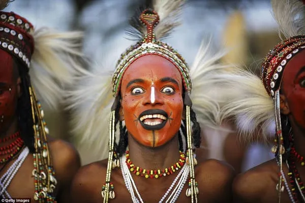 alt text: Chàng trai bộ tộc Wodaabe tham gia cuộc thi sắc đẹp. Anh chàng trang điểm cầu kỳ với đôi mắt trắng và hàm răng trắng, cười tươi để thu hút sự chú ý của các cô gái. Đây là một phần của lễ hội Gerewol, nơi phụ nữ Wodaabe lựa chọn chồng.