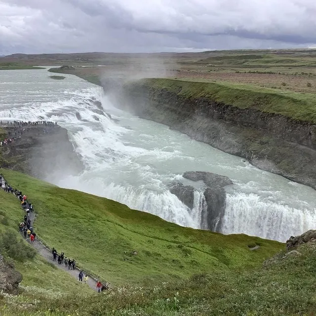 alt text: Dòng nước của thác Gullfoss đổ xuống tạo thành một lớp sương mù dày đặc, dưới ánh nắng mặt trời tạo nên cầu vồng tuyệt đẹp.