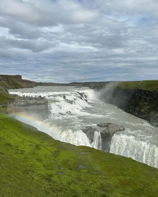alt text: Hình ảnh cận cảnh thác nước Gullfoss cho thấy sức mạnh của dòng nước đổ xuống từ trên cao, tung bọt trắng xóa. Xung quanh là khung cảnh thiên nhiên hoang sơ với những vách đá dựng đứng và thảm thực vật xanh mướt.