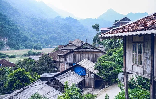 alt text: Khung cảnh bình minh trên hồ Ba Bể với mặt nước yên ả, mây trời trong xanh và những dãy núi trùng điệp phía xa. Một chiếc thuyền nhỏ đang neo đậu trên mặt hồ tạo nên một bức tranh thiên nhiên tuyệt đẹp.