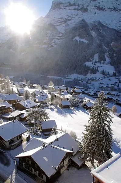 alt text: Làng Grindelwald, Thụy Sĩ, nằm dưới chân dãy núi Alps hùng vĩ, được bao quanh bởi những đỉnh núi phủ đầy tuyết trắng. Những ngôi nhà gỗ truyền thống với mái che phủ tuyết tạo nên một khung cảnh đẹp như trong truyện cổ tích.
