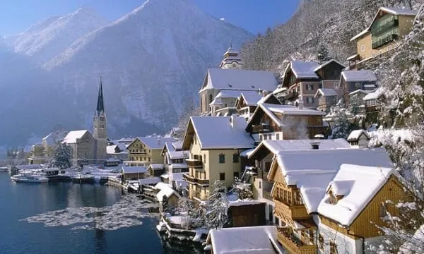 alt text: Ngôi làng Hallstatt, Áo, nằm bên hồ nước trong veo, được bao quanh bởi những dãy núi phủ đầy tuyết trắng. Những ngôi nhà nhỏ xinh với kiến trúc truyền thống tạo nên một khung cảnh đẹp như tranh vẽ.