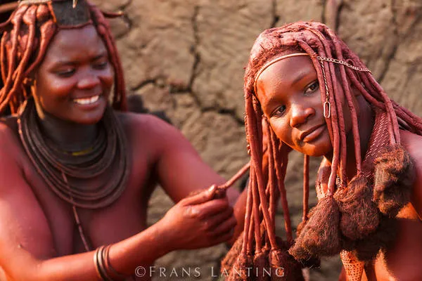 alt text: Phụ nữ Himba với làn da và mái tóc màu đỏ đặc trưng. Họ sử dụng hỗn hợp otjize làm từ bơ, mỡ và đất đỏ để tạo nên màu sắc này.