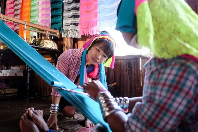 alt text: Phụ nữ Kayan dệt vải và trò chuyện với du khách