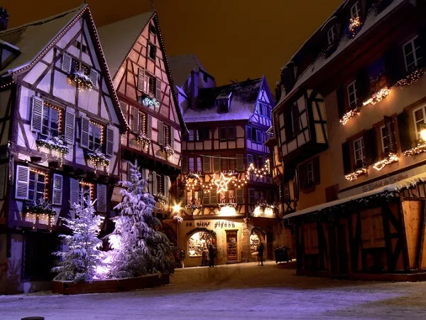 alt text: Thị trấn Colmar, Pháp, với những ngôi nhà gỗ cổ kính, mái ngói đủ màu sắc và những con đường lát đá quanh co. Tuyết trắng phủ kín mái nhà và đường phố, tạo nên một khung cảnh lãng mạn và ấm áp.