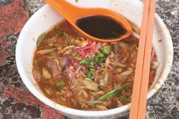 alt text: Tô mì Assam Laksa với nước dùng đỏ cam, cá và rau thơm