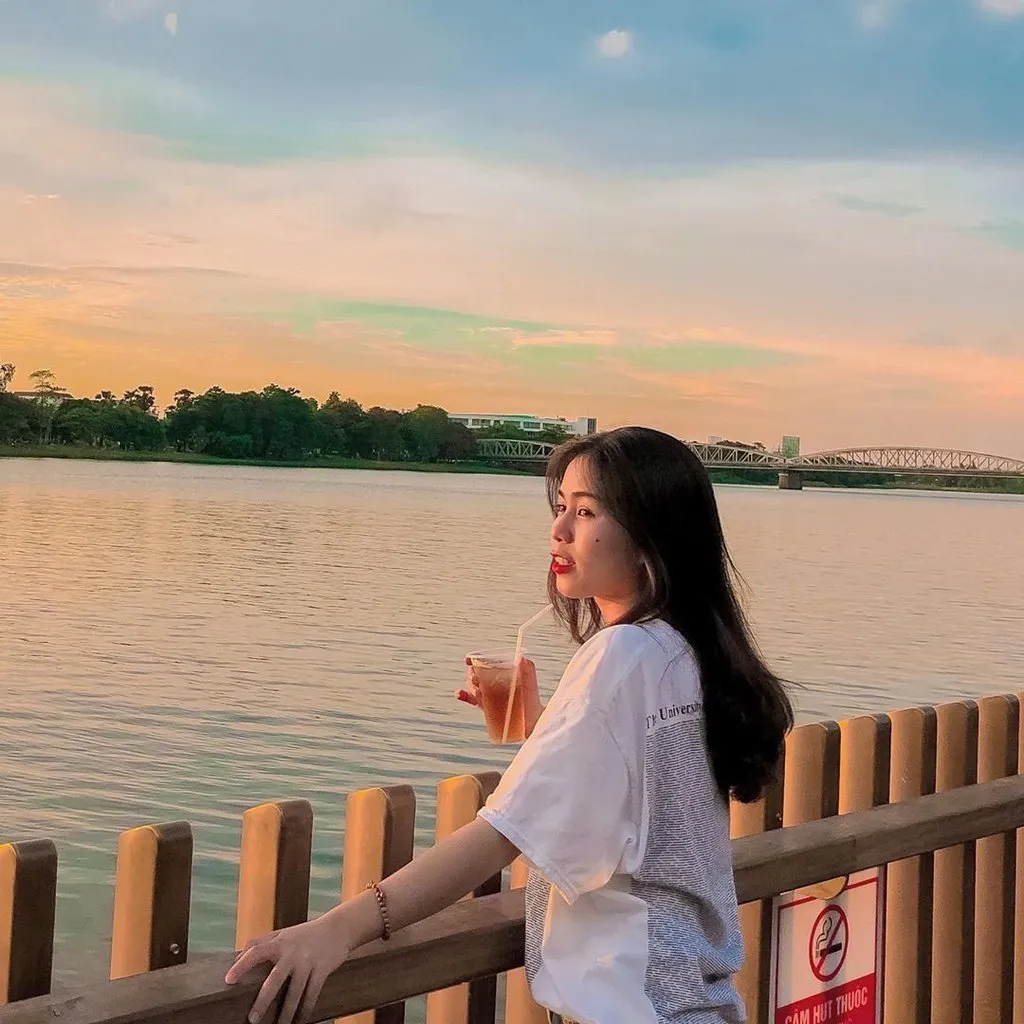 Cầu gỗ lim bên bờ sông Hương lúc hoàng hôn với ánh nắng vàng cam phủ lên mặt nước và không gian xung quanh.