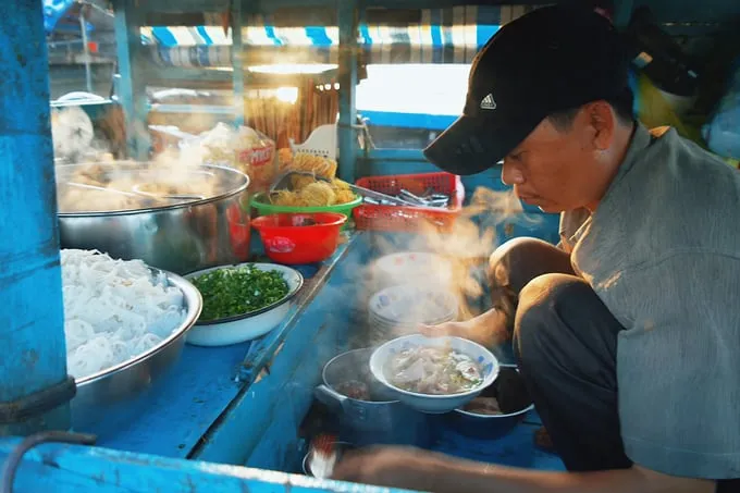 Du khách thưởng thức bữa sáng trên thuyền, người bán hàng dùng móc sắt để đưa đồ ăn qua.