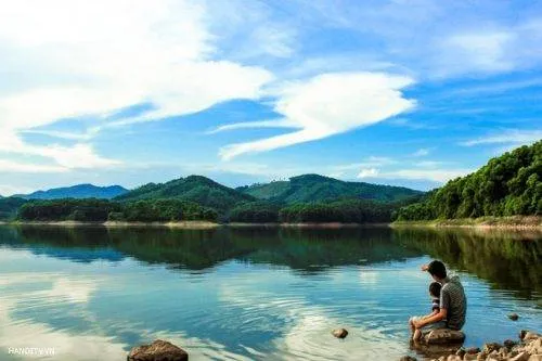 Hình ảnh thuyền du lịch trên Hồ Núi Cốc, phía xa là núi non hùng vĩ. Du khách có thể trải nghiệm cảm giác thư thái khi du ngoạn trên hồ.