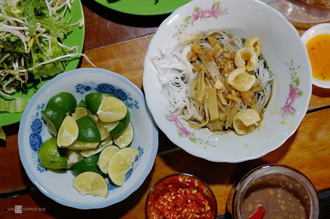 Tô bún mắm cua đầy đủ với bún, nước dùng đen, da heo chiên giòn, măng le, hành phi và đậu phộng, ăn kèm với rau sống tươi mát.